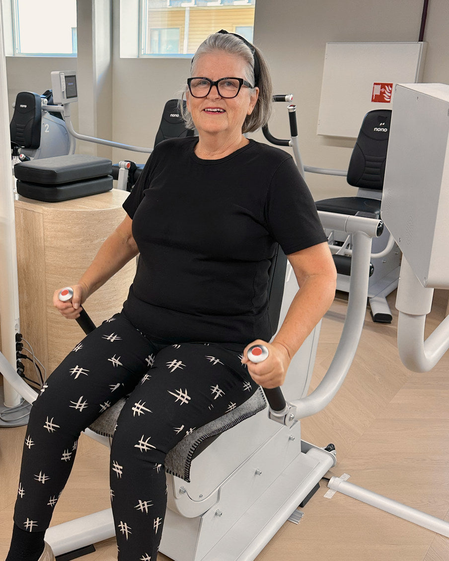 Det samme medlemmet presser håndtakene ned ved hoftene i biceps- og tricepsmaskinen.