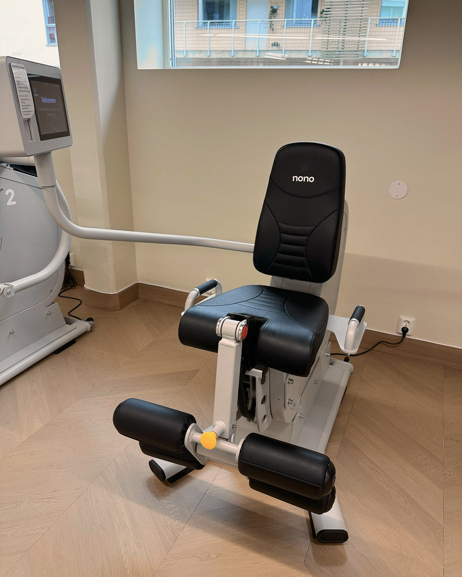 Maskinen for beinstrekk og beinbøy står tom under vinduet, med to rullepølser og gul justeringsknott.