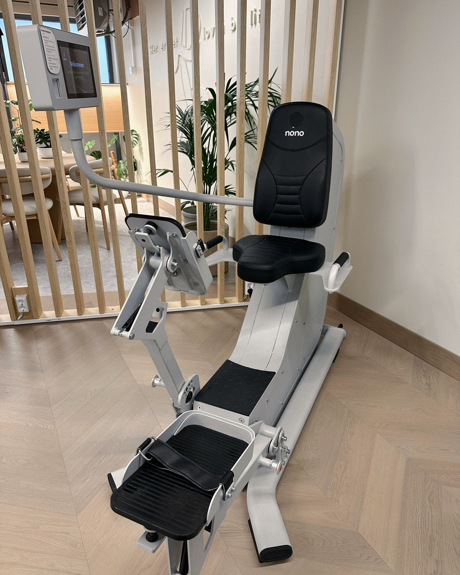 Beinpressen står tom foran spileveggen, med to fotplater og planter bak.