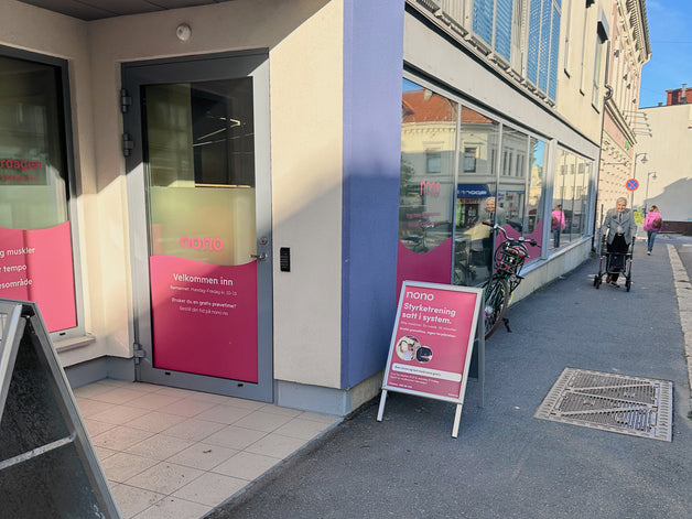 Inngangen til Nono i Kongens gate 25A i Moss: en glassdør med rosa folie og teksten «Velkommen inn», et rosa skilt på fortauet og to forbipasserende lenger nede i gata.