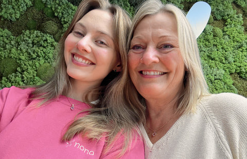 To kvinner tar en selfie kinn mot kinn foran en vegg av mose. Den ene har rosa Nono-genser.
